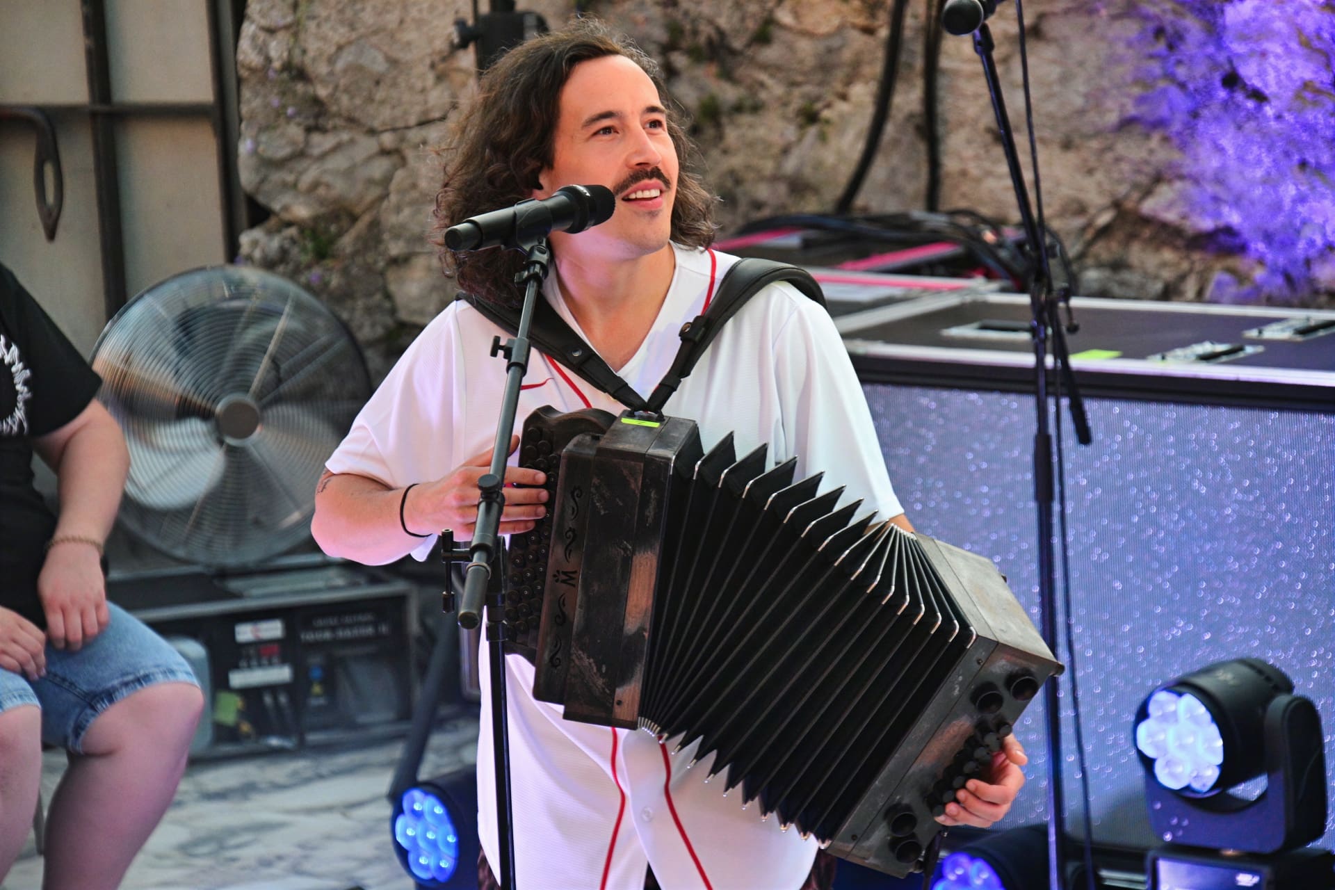 Ein Mann mit langen Haaren spielt Akkordeon und singt in ein Mikrofon auf der Bühne