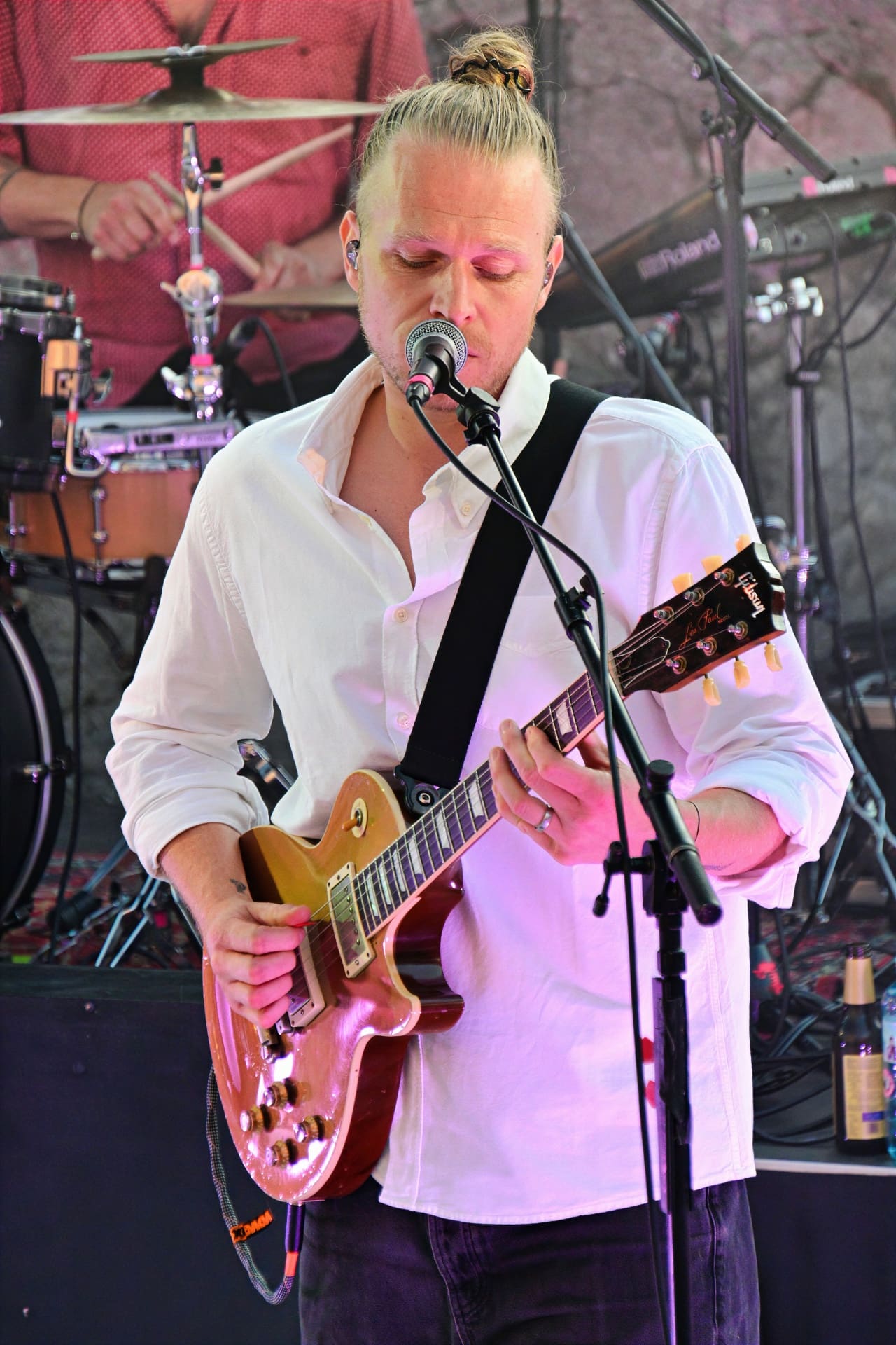 Ein blondhaariger Musiker mit Dutt spielt E-Gitarre und singt auf einer Bühne.