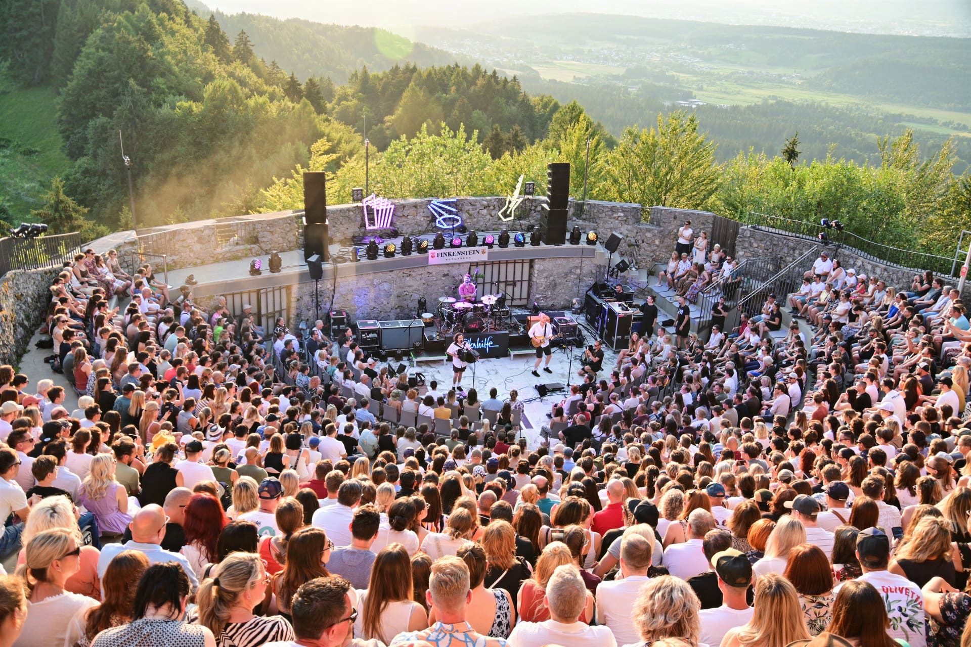 Große Menschenmenge bei einem Open-Air-Konzert auf der Burgarena Finkenstein mit Blick auf die Bühne und Berge