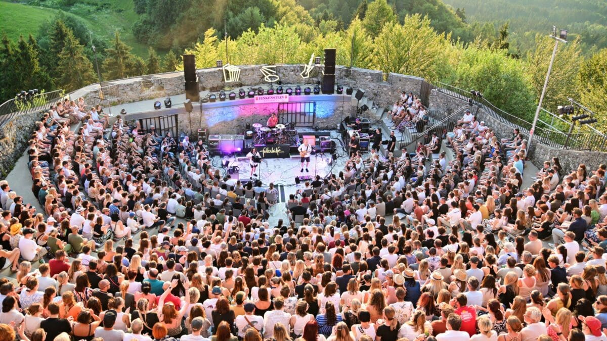Eventbesucher sitzten vor der Konzertbühne mit Band in bewaldeter Landschaft