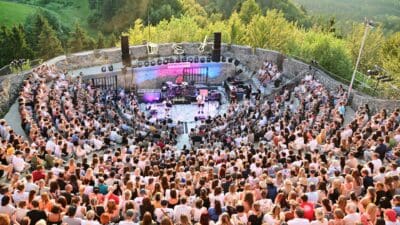 Eventbesucher sitzten vor der Konzertbühne mit Band in bewaldeter Landschaft
