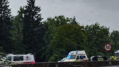 Rettungswagen und Polizeifahrzeuge stehen auf nasser Straße bei Regen vor Bäumen