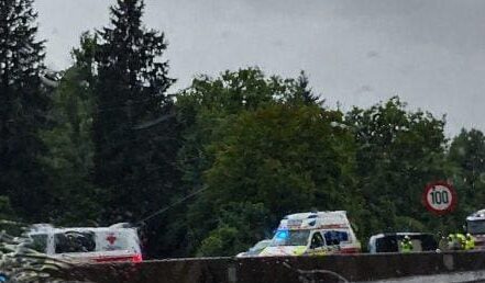 Rettungswagen und Polizeifahrzeuge stehen auf nasser Straße bei Regen vor Bäumen