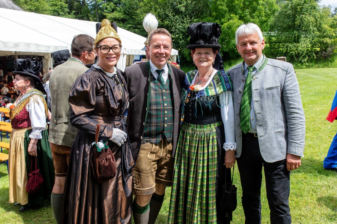 Gruppe von Erwachsenen in traditioneller Kärntner Tracht posiert lächelnd auf einer Wiese vor Zelten