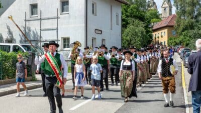 Festzug mit Trachtenträgern, Blaskapelle und Stabträger auf einer Straße