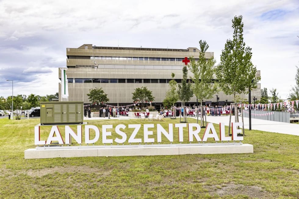 Großer weißer Schriftzug Landeszentrale vor modernem Gebäude mit Rotkreuz-Logo und feiernden Menschen in Graz