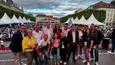 Gruppe von Menschen posiert auf einer Bühne vor einer großen Menschenmenge beim Public Viewing in Klagenfurt