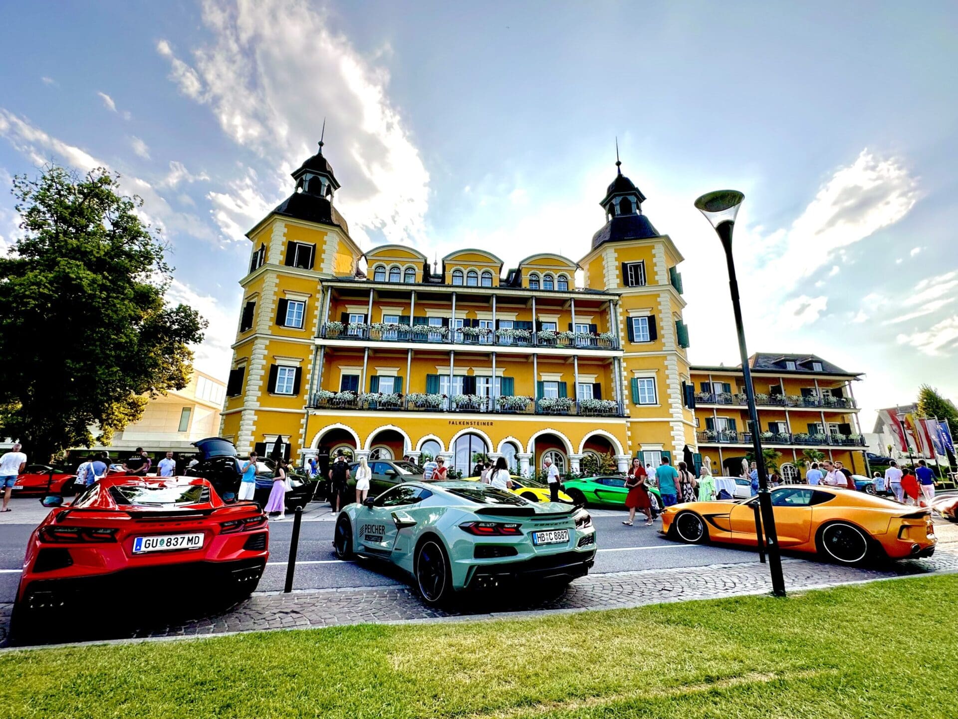 Rote, hellgrüne und orangefarbene Sportwagen vor einem großen gelben Hotel mit Türmen