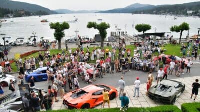 Menschenmenge um bunte Sportwagen am Ufer eines großen Sees