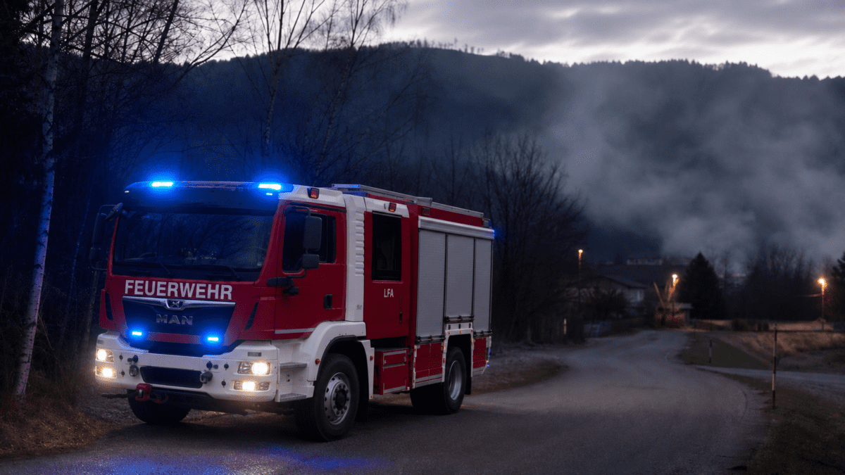 Rotes Feuerwehrfahrzeug mit blauem Blaulicht auf nebliger Landstraße vor Bergen