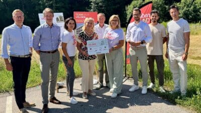 Gruppe von Menschen bei der Präsentation des Teamhauses Velden mit Schildern im Freien