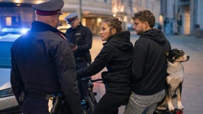 Polizist spricht mit Radfahrerin auf Fahrrad mit Mann und Hund auf dem Gepäckträger