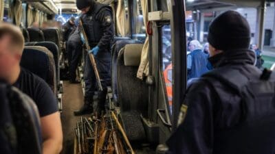 Polizisten stehen in einem Reisebus neben vielen beschlagnahmten Gewehren auf dem Boden