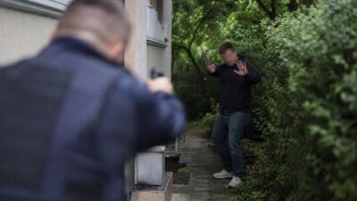 Polizist mit gezogener Waffe zielt auf einen Mann mit Küchenmesser in einem Garten