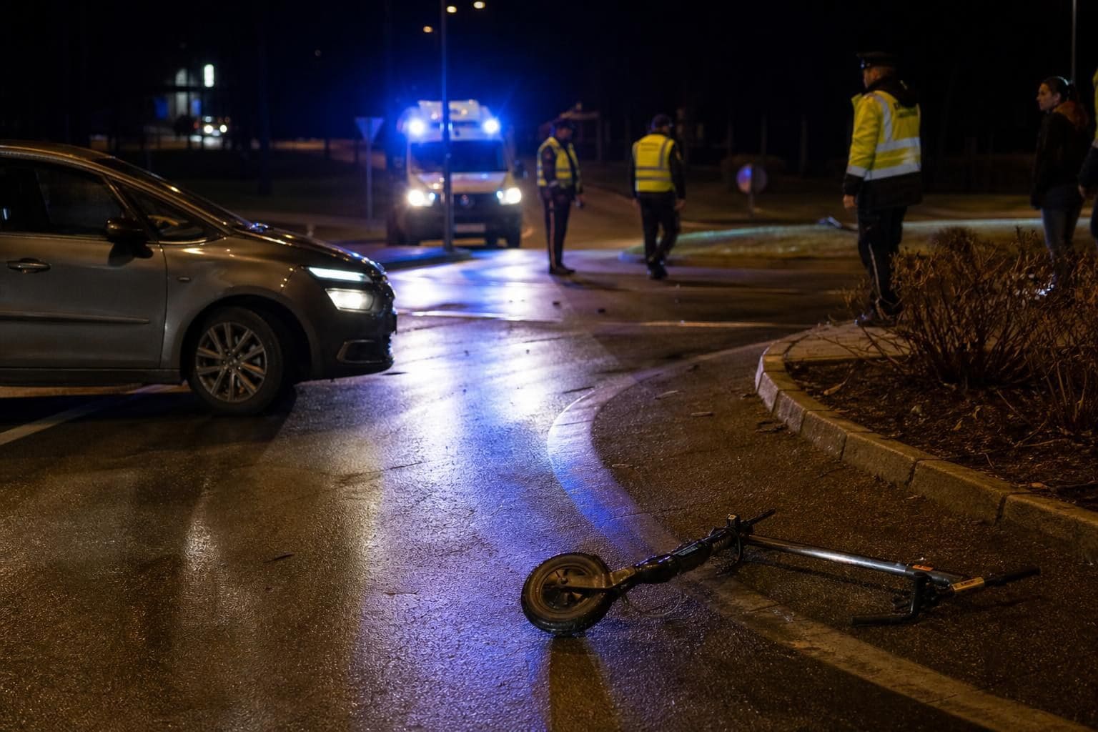 Umgestürzter E-Scooter liegt nach Unfall im Kreisverkehr auf nasser Straße bei Nacht
