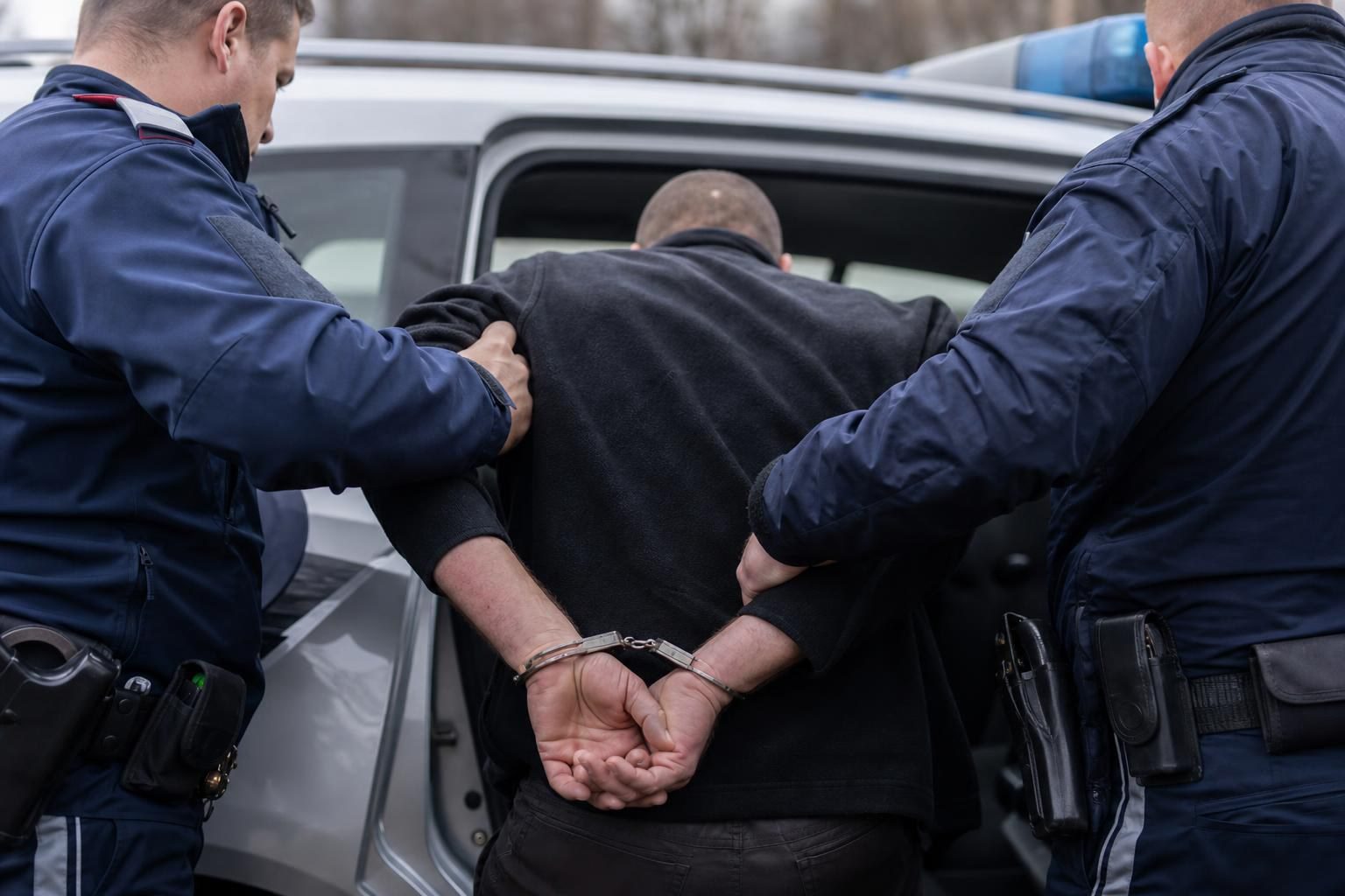 Zwei Polizisten in blauen Uniformen führen einen in Handschellen gefesselten Mann zu einem Einsatzfahrzeug