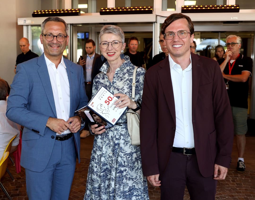 Drei Personen bei der Eröffnung der Tage der deutschsprachigen Literatur in Klagenfurt, Frau hält Buch zum Bachmannpreis.