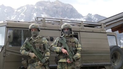 Zwei Soldaten in Tarnuniform und Helmen mit Gewehren vor einem Militärfahrzeug in den Bergen