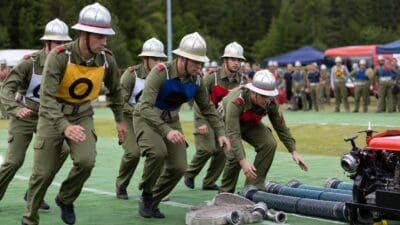 Feuerwehrleute in grünen Uniformen mit bunten Schürzen laufen auf grünem Rasen