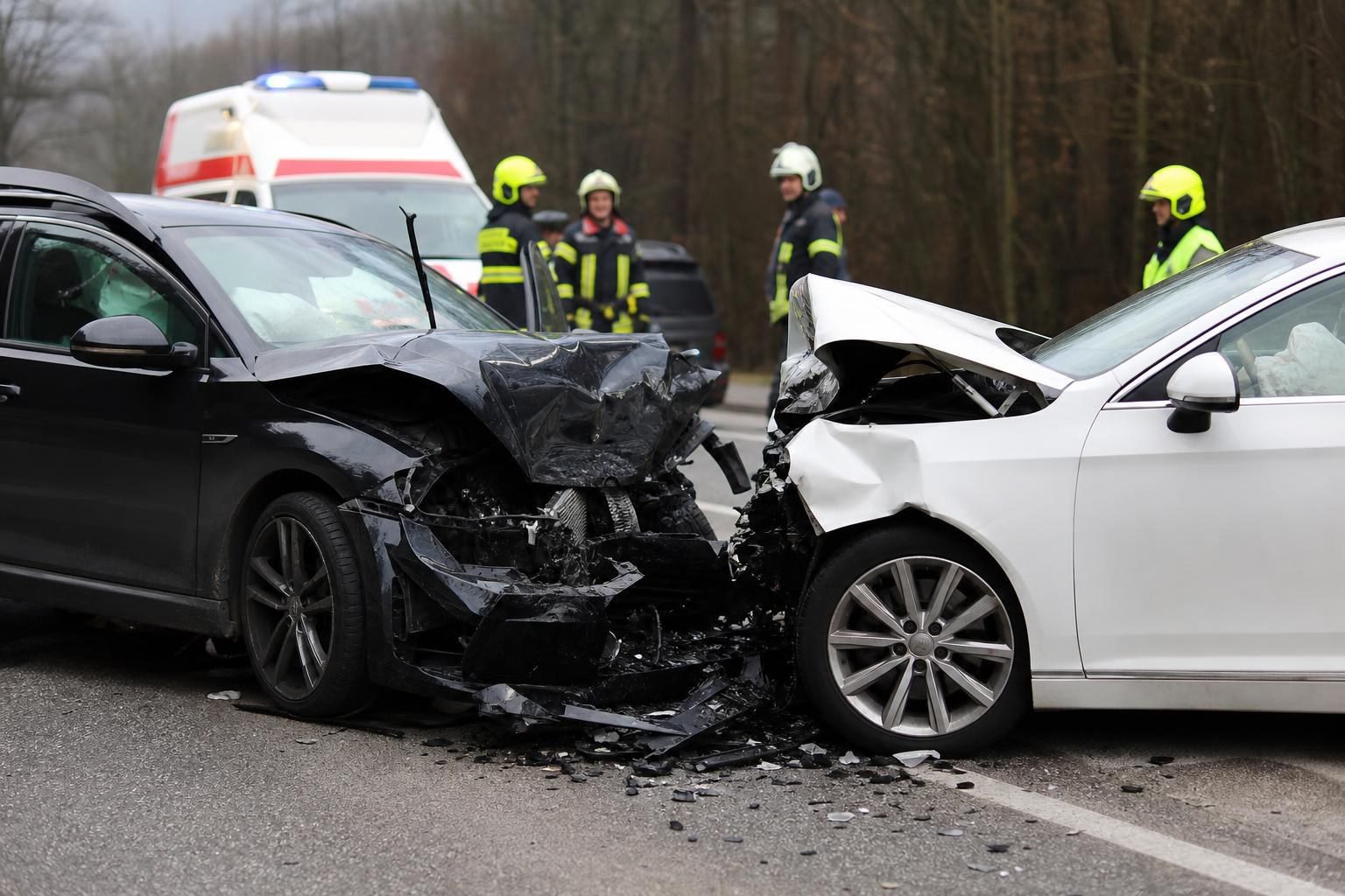 Zwei stark beschädigte Autos nach einem Frontalzusammenstoß auf einer Straße mit Rettungskräften im Hintergrund