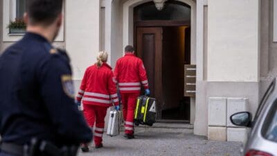 Rettungskräfte in roten Uniformen betreten mit Koffern ein Wohnhaus
