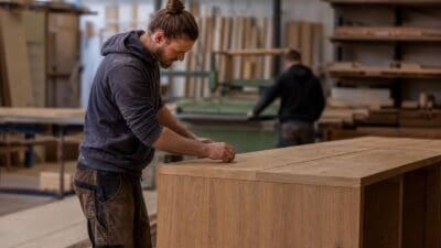 Tischler mit Dutt und Bart bearbeitet eine Holzplatte in der Werkstatt
