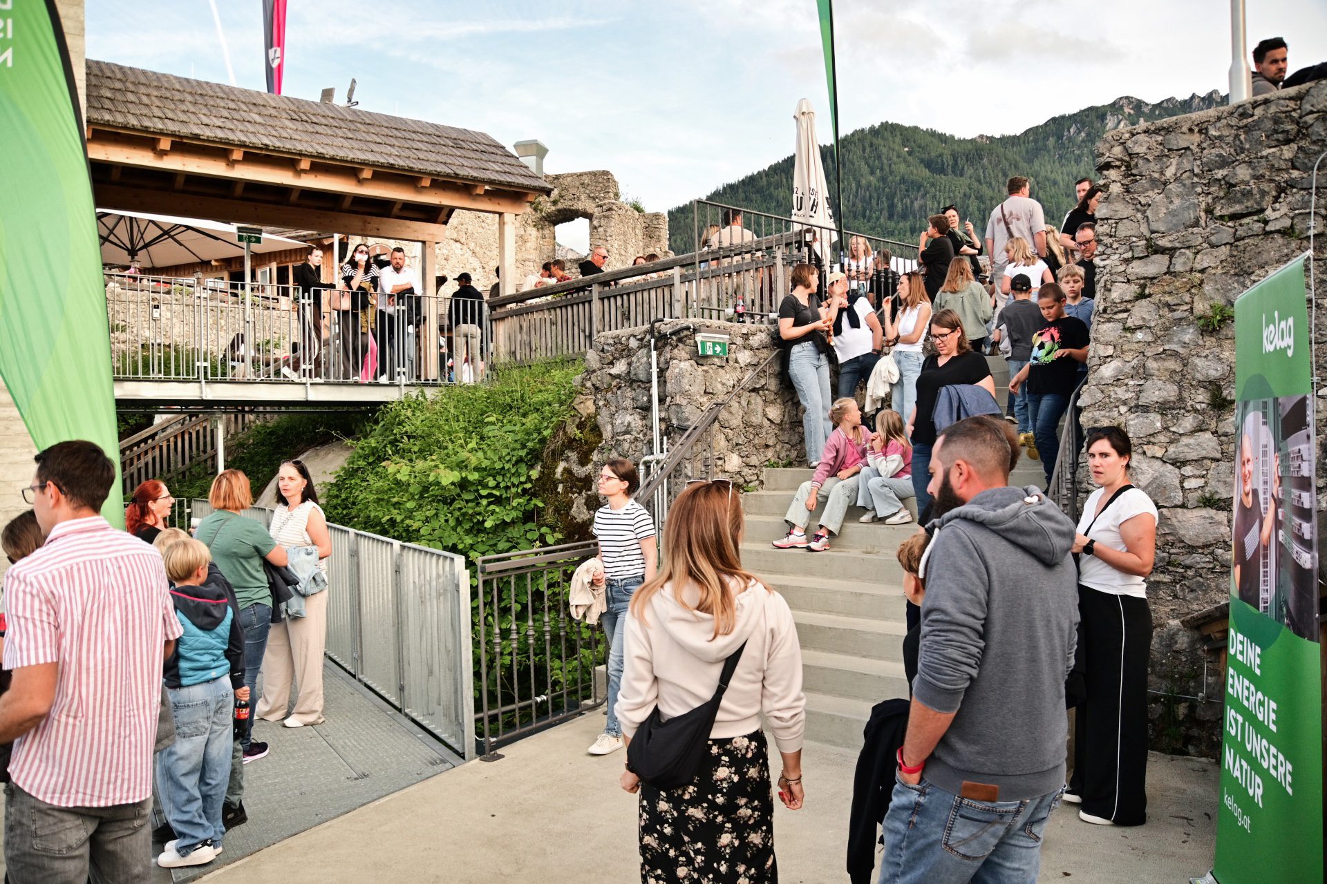 Menschenmenge versammelt sich auf einer Treppe vor einer historischen Steinmauer mit Bergen im Hintergrund