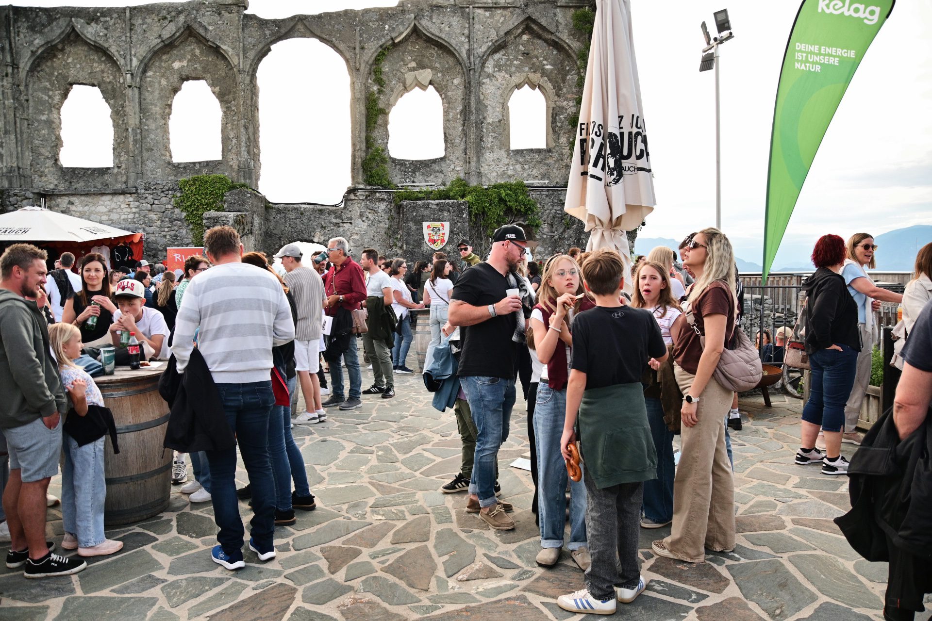 Menschenmenge steht auf Steinpflaster vor alter Burgruine mit großen Bögen