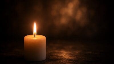 Eine brennende weiße Kerze auf dunkler Oberfläche mit warmem Lichtschein