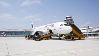 Weißes Eurowings Flugzeug am Flughafen Klagenfurt mit gelber Fluggastbrücke und Gepäckwagen