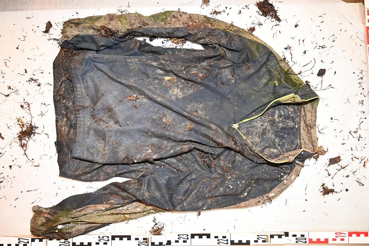 Verschmutztes dunkelblaues Radtrikot mit grünen Akzenten auf weißer Unterlage mit Maßstab