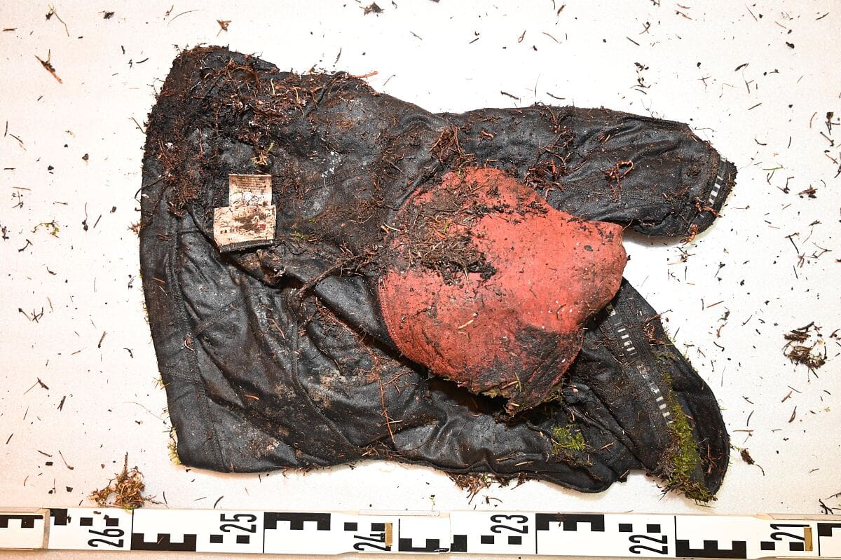 Verschmutztes schwarzes Radtrikot mit rotem Polster und Etikett auf weißer Fläche neben Zentimetermaßband