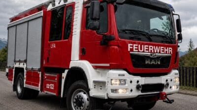 Rotes und weißes Feuerwehrfahrzeug der Marke MAN mit Blaulicht auf einer Straße im Nebel