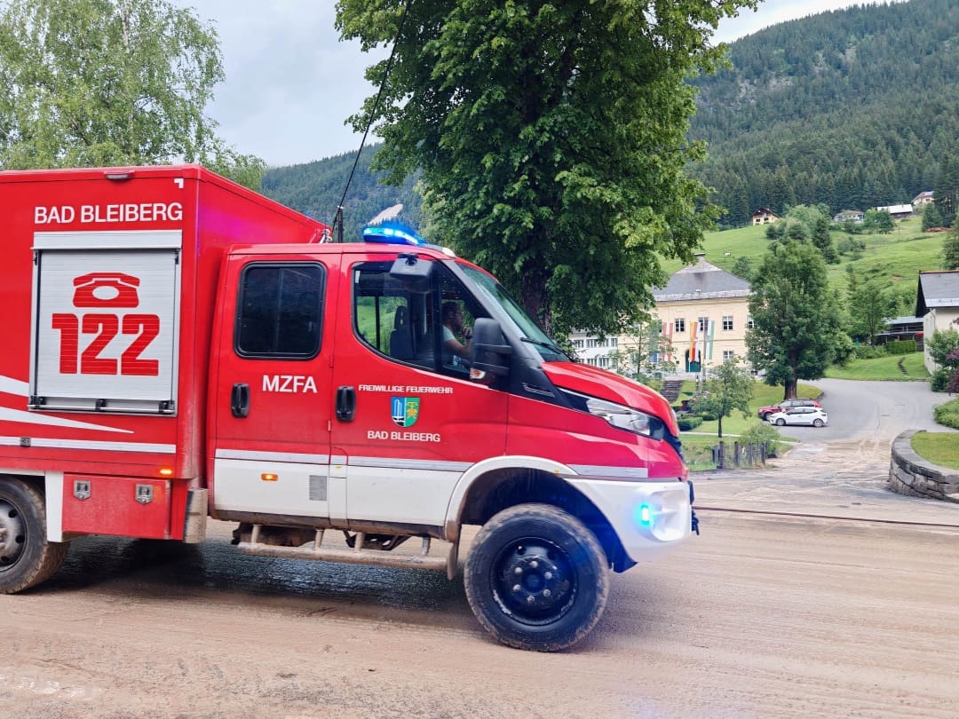 Rotes Feuerwehrfahrzeug der Freiwilligen Feuerwehr Bad Bleiberg auf schlammiger Straße mit Blaulicht