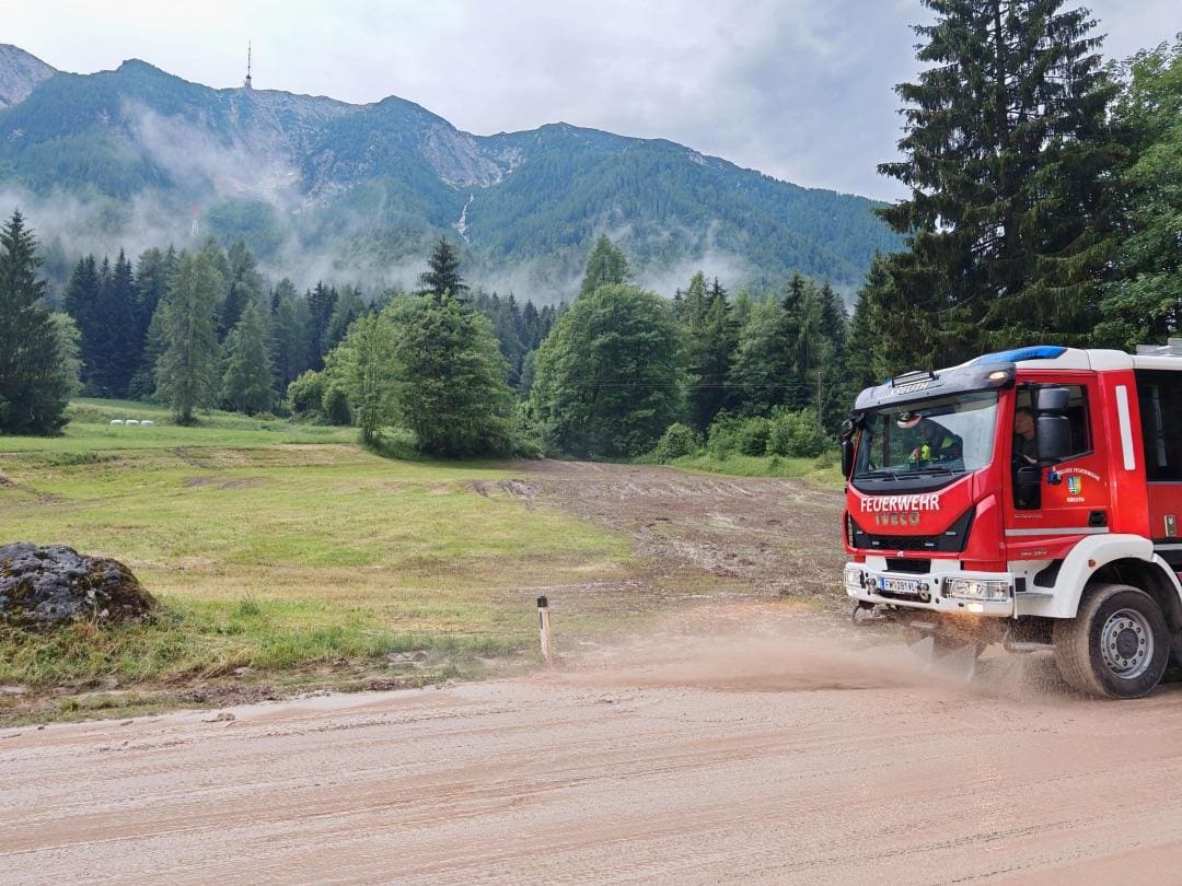 Rotes Feuerwehrfahrzeug fährt auf schlammiger Straße in bergiger Landschaft mit Nebel