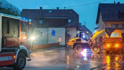 Feuerwehrfahrzeug, gelber Radlader und Lkw auf nasser Straße bei Dämmerung