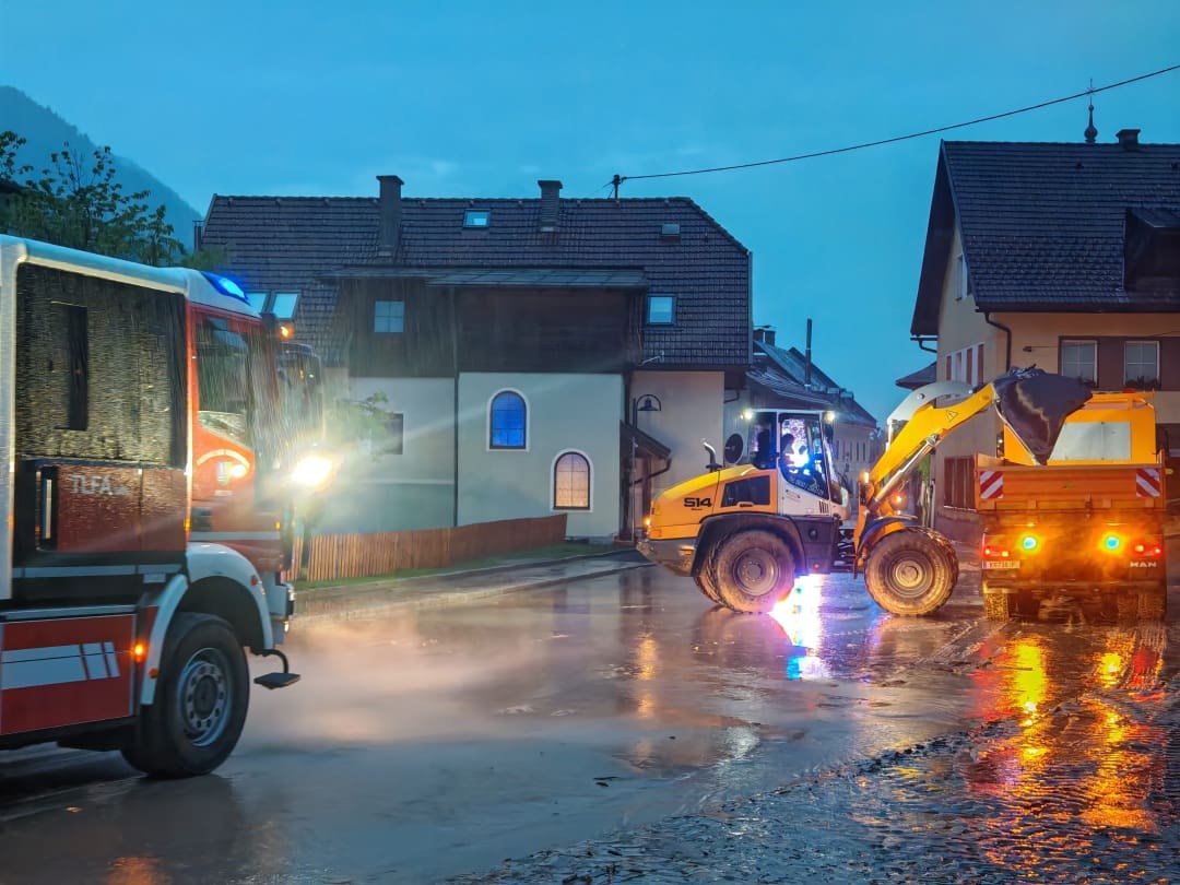 Feuerwehrfahrzeug, gelber Radlader und Lkw auf nasser Straße bei Dämmerung