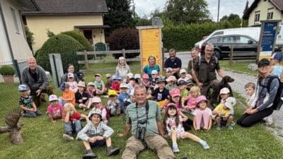 Kinder und Betreuer des Kindergartens sitzen auf einer Wiese beim Themenweg in Lieserbrücke.