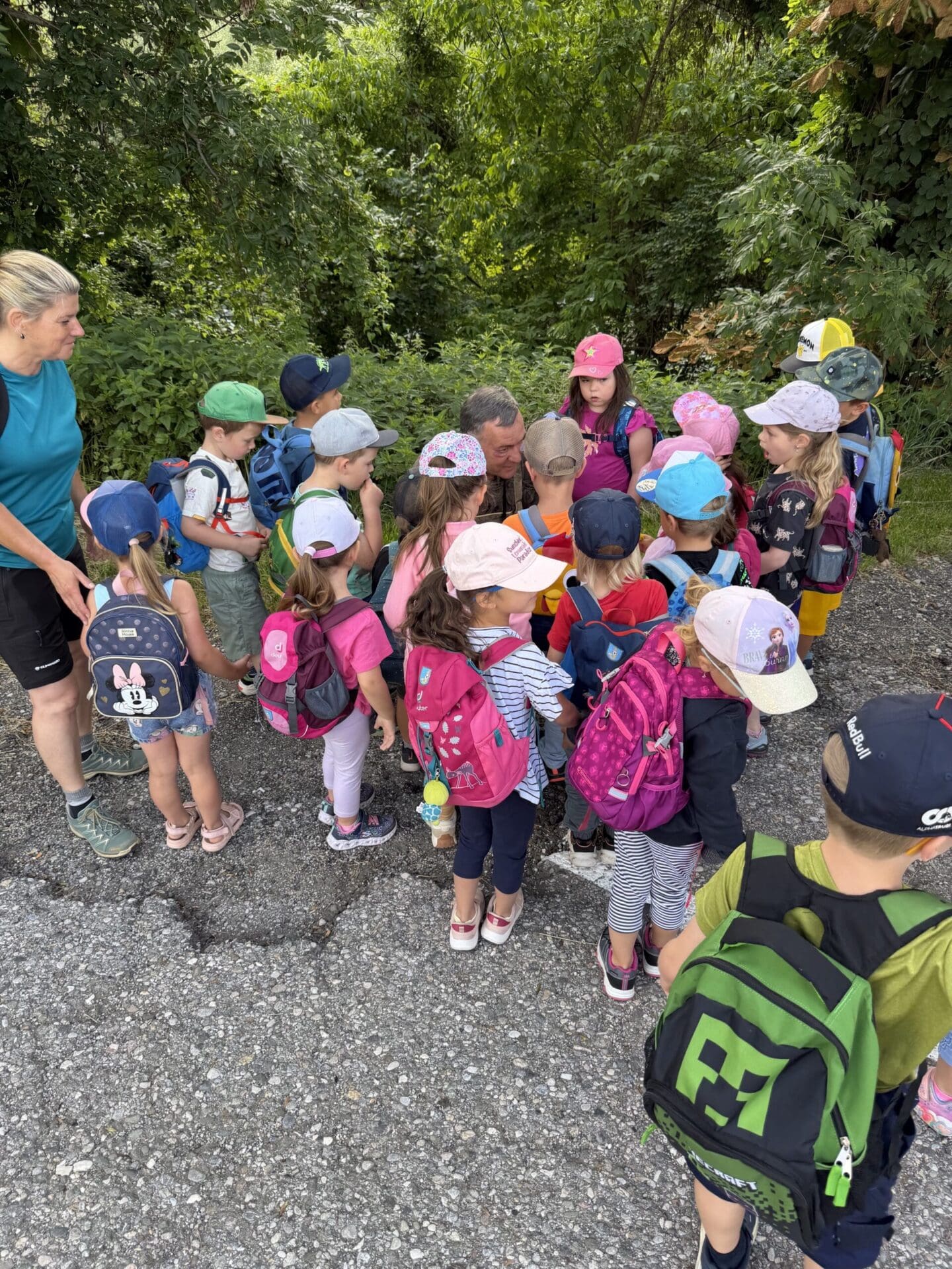 Gruppe von Kindergartenkindern mit bunten Rucksäcken und Mützen auf einem Kiesweg