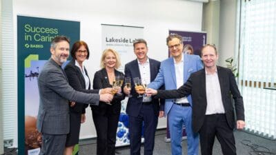 Sechs Personen in Geschäftskleidung stoßen mit Sektgläsern in einem Konferenzraum an.