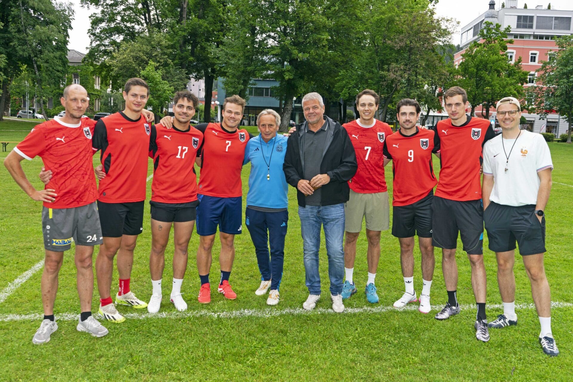 Gruppe von Fußballspielern in roten Trikots und weiteren Personen auf einem Rasenplatz