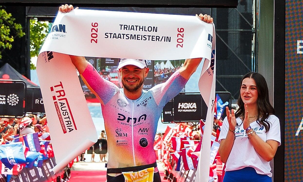 Lachender Triathlet in buntem Anzug hält Banner über dem Kopf neben klatschender Frau