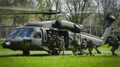 Soldaten in Tarnuniform steigen aus einem militärischen Hubschrauber auf einer Wiese aus