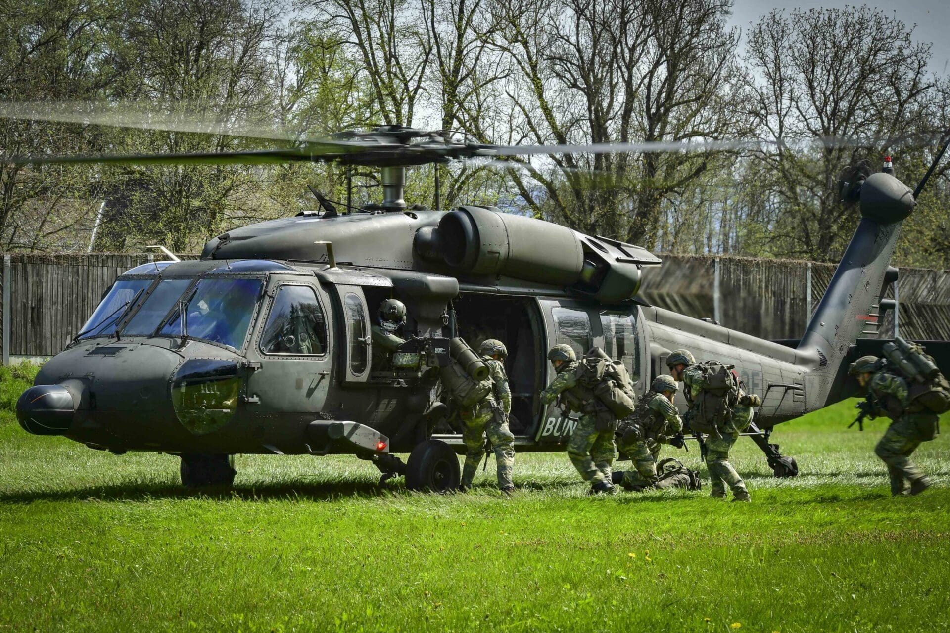 Soldaten in Tarnuniform steigen aus einem militärischen Hubschrauber auf einer Wiese aus