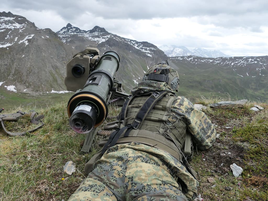 Soldat in Tarnuniform liegt auf einem Berg und bedient einen schweren Raketenwerfer vor einer Berglandschaft