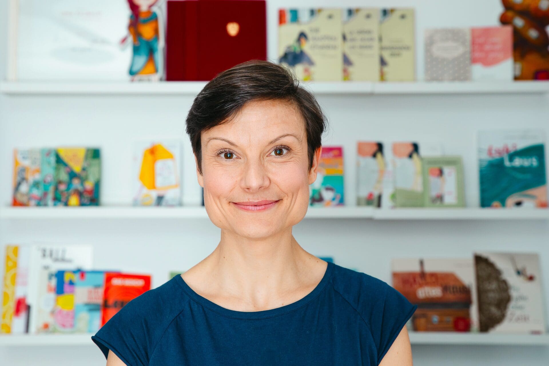 Porträt von Lena Raubaum mit kurzen dunklen Haaren vor einem Bücherregal mit Kinderbüchern