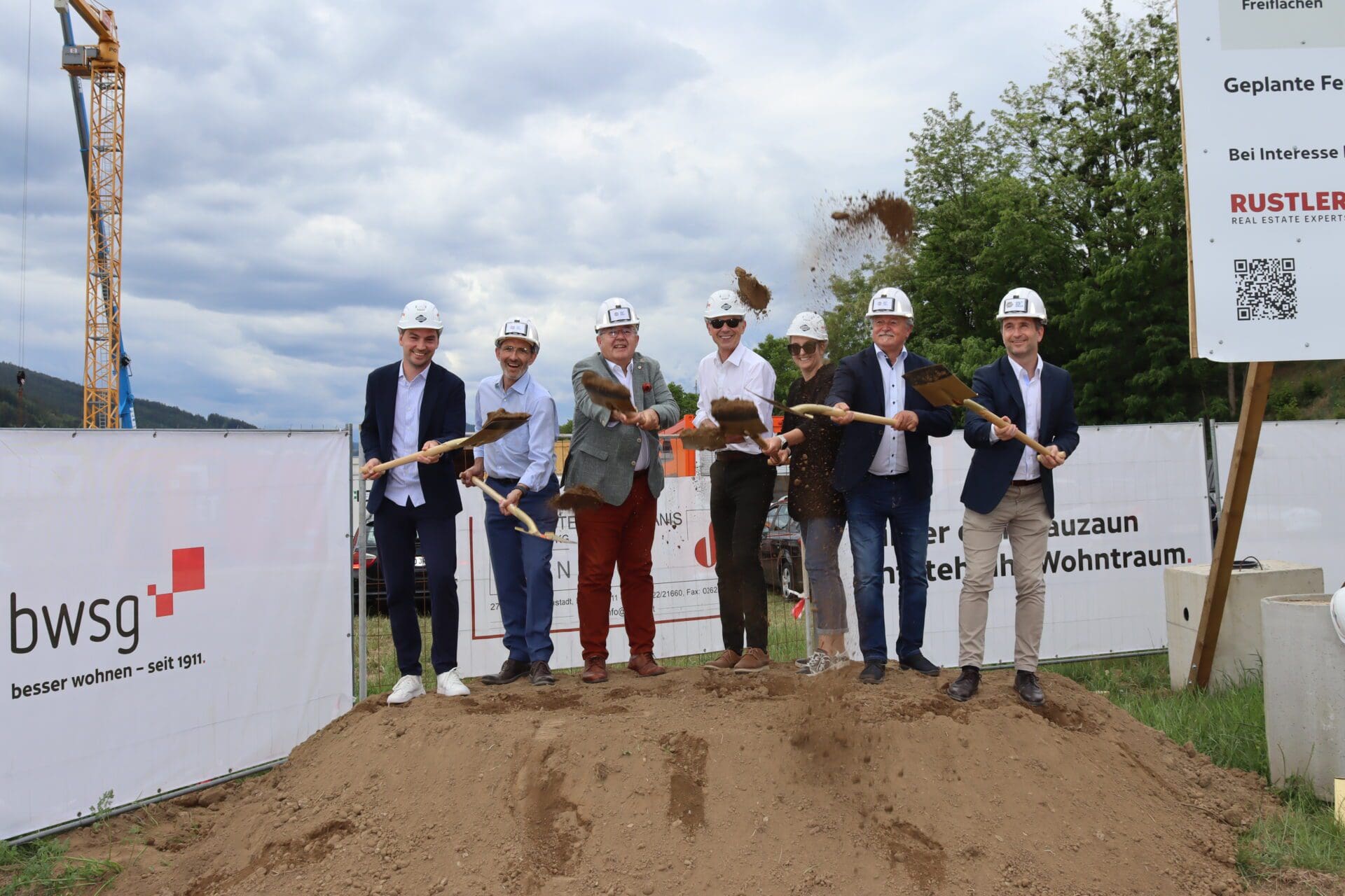 Gruppe von Personen in Schutzhelmen beim Spatenstich auf einer Baustelle