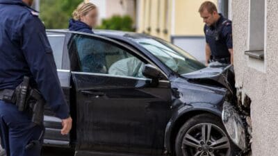 Polizisten untersuchen ein schwarzes Auto, das gegen eine Hauswand gefahren ist