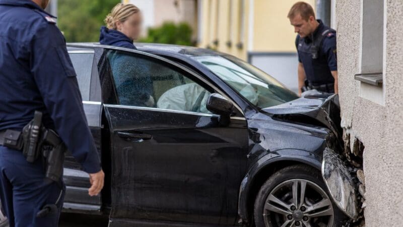 Polizisten untersuchen ein schwarzes Auto, das gegen eine Hauswand gefahren ist