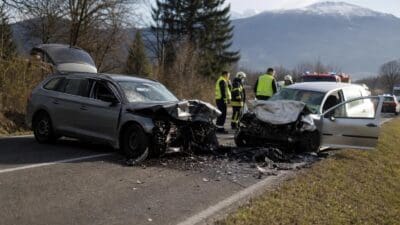 Zwei stark beschädigte Pkw nach Frontalcrash auf Landstraße mit Rettungskräften im Hintergrund